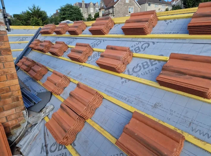 A re-roof in progress: new felt and battens fitted, with stacks of red tiles loaded out ready to lay