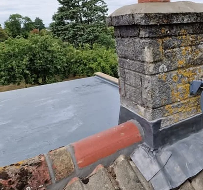 A flat roof surface meeting a chimney finished with lead flashing
