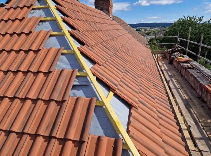 A long roof being re-tiled with new battens and red tiles