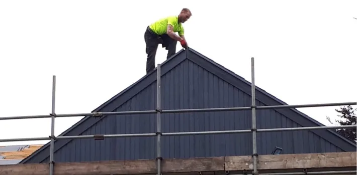 A roofer in hi-vis working at the top of a gable