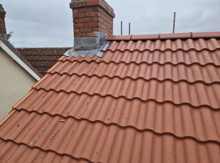 A red tiled roof with lead flashing around a brick chimney
